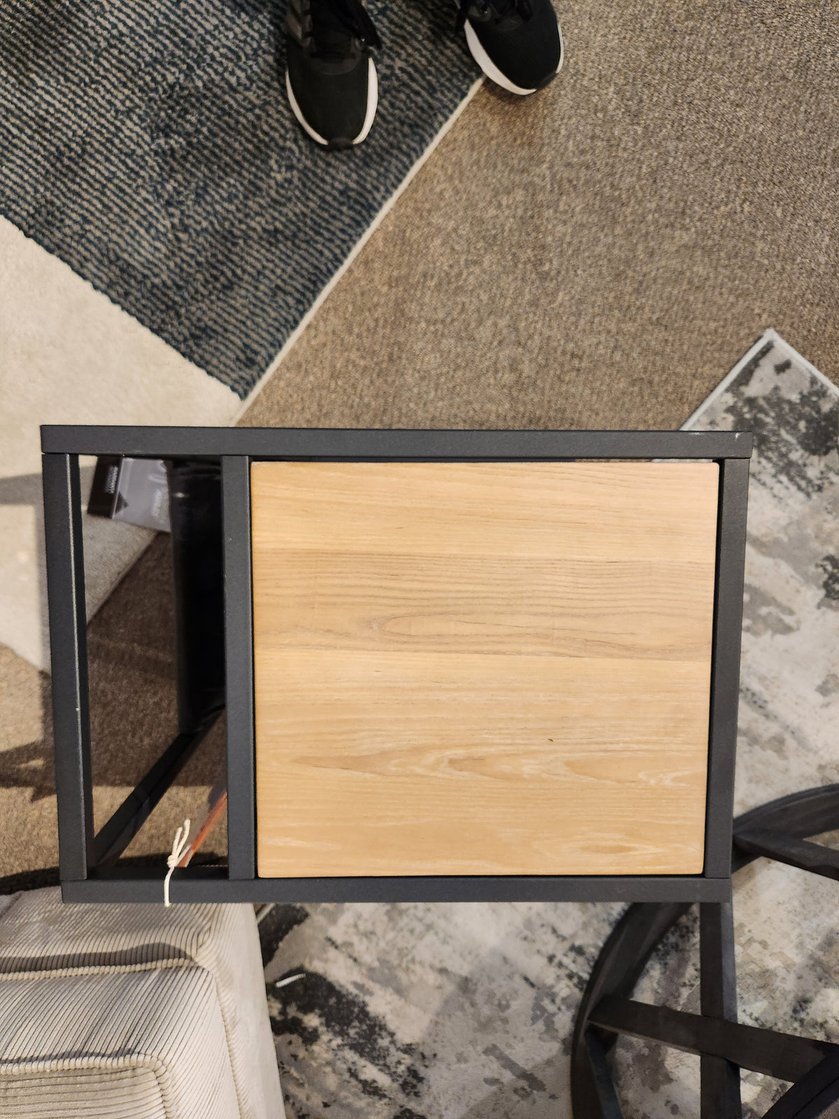 Top view of Ashley's Freslowe T931 end table with elm veneer and matte black frame on patterned carpet. Sneakers visible.