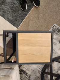 Top view of Ashley's Freslowe T931 end table with elm veneer and matte black frame on patterned carpet. Sneakers visible.