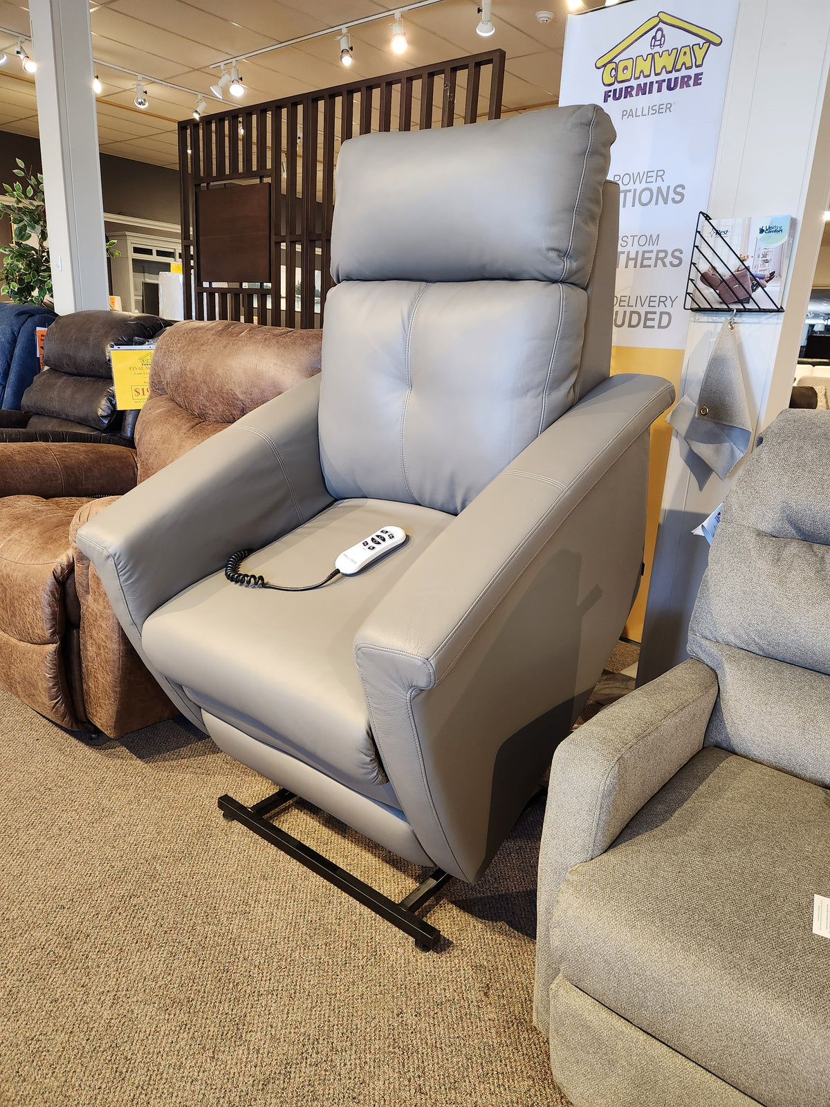 The Granville furniture store showroom features the Palliser Granville 40183-B2 Power Lift Chair in gray, with a remote control resting on the seat, seamlessly blending style and comfort.