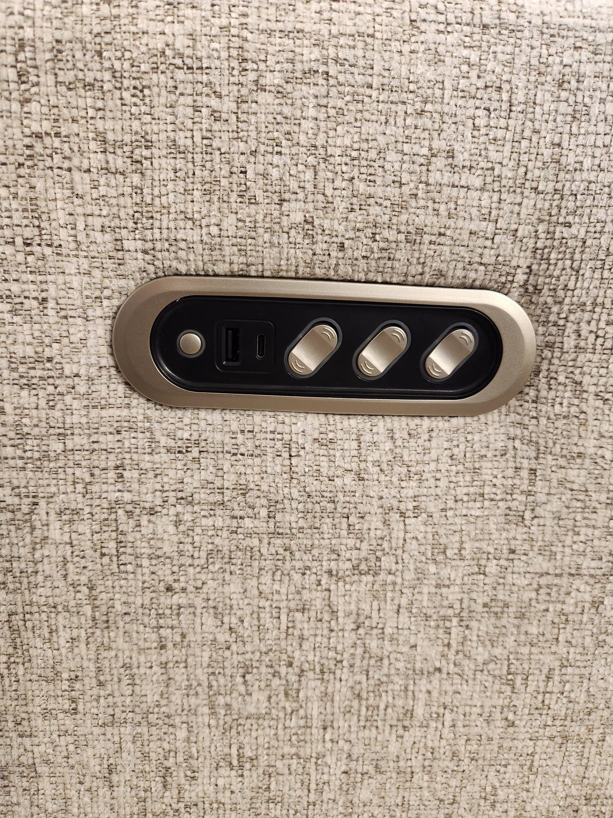 Close-up of a metallic panel featuring three switches and a USB port resting on a textured fabric surface, highlighting the exquisite upholstery of the Decor-rest M8500 Power Reclining Loveseat, crafted in Canada.