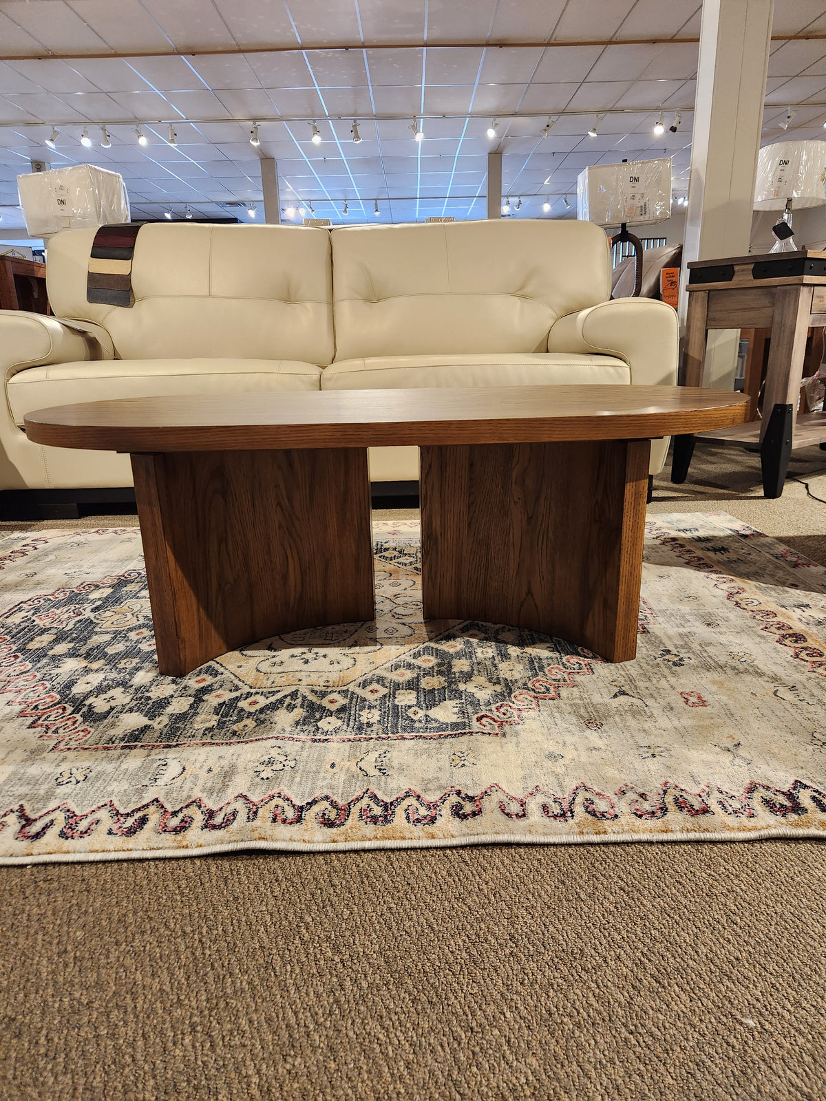 The Austanny T683 Coffee Table by Ashley graces the decorative rug, perfectly complementing the white sofa in a stylish showroom setting.