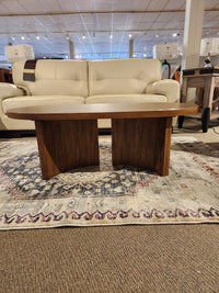 The Austanny T683 Coffee Table by Ashley graces the decorative rug, perfectly complementing the white sofa in a stylish showroom setting.