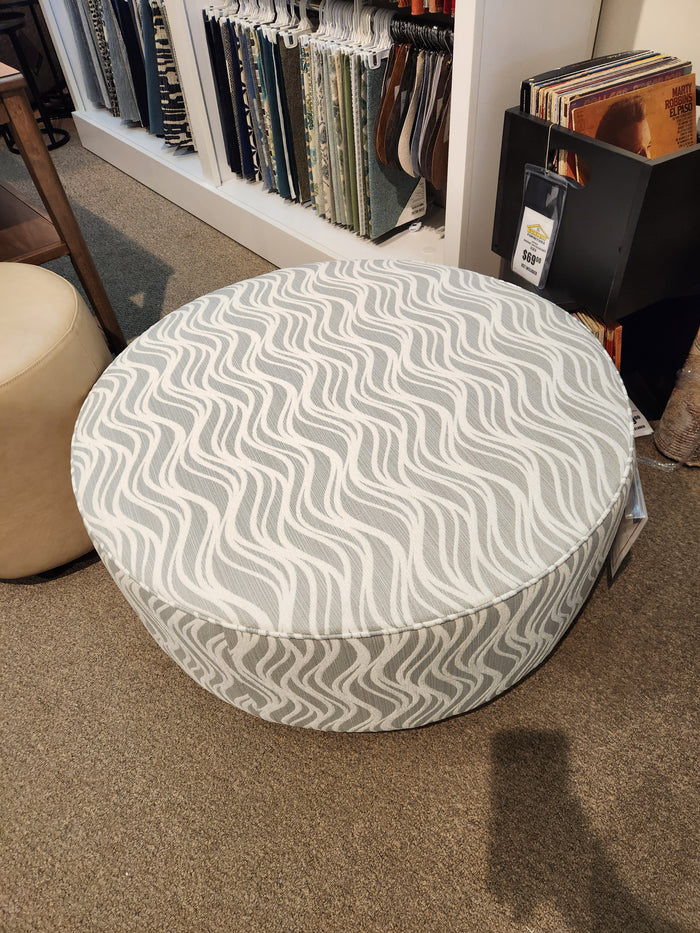 Palliser's 77004 Mingle Medium Round Ottoman features a gray and white wavy pattern on carpet by fabric samples and vinyl records.