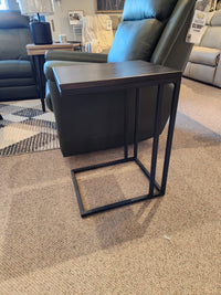 The AlaCarte Snack Table by Handstone features a dark wood top and black metal frame, perfect beside a recliner on carpet.