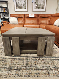 A Magnussen T5865 Conrad gray pie-shaped cocktail table sits on a rug in front of a sectional.