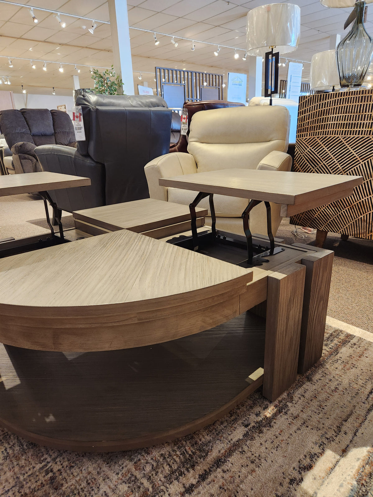 Furniture showroom with a beige armchair, dark recliner, and Magnussen's T5865 Conrad Pie Shaped Cocktail Table (Pine Solids).