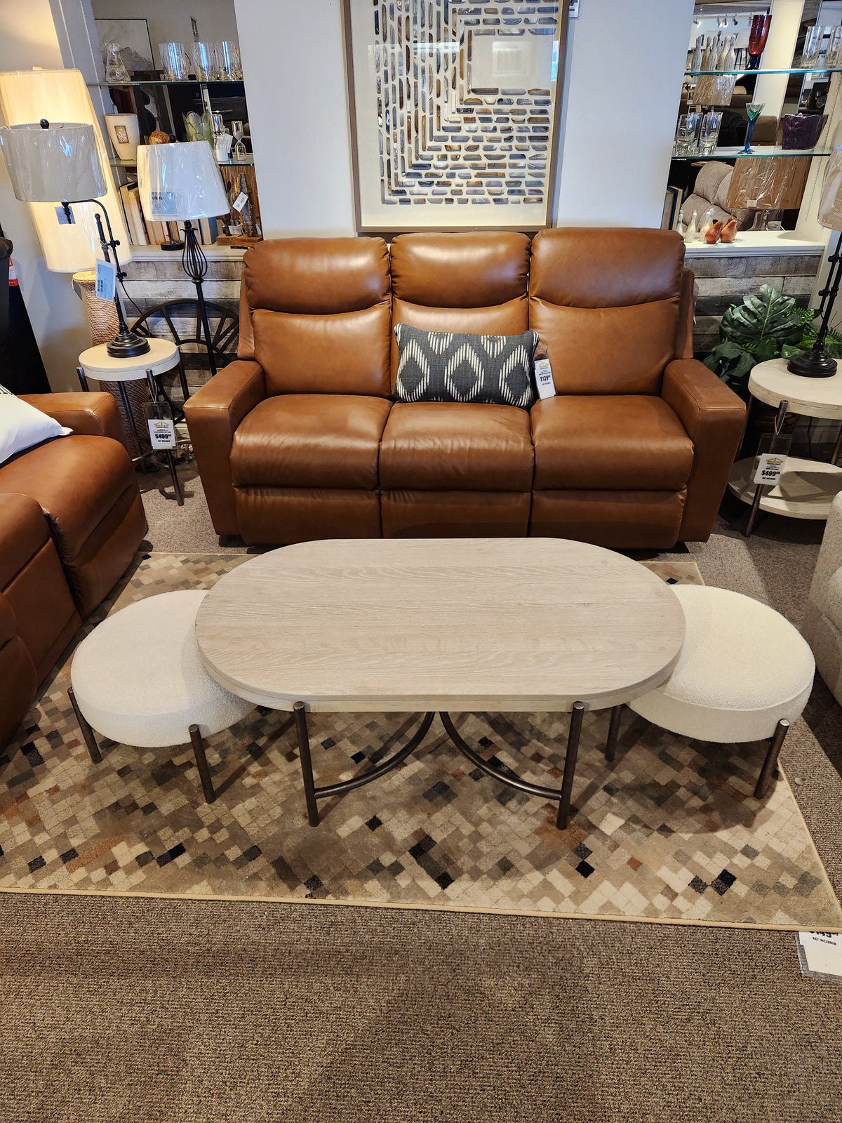 Living room setup with a brown leather sofa, Magnussen's Jennings Oval Coffee Table in Edgecomb Grey on a patterned rug.