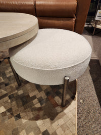 Round white chair with antique nickel legs next to the Magnussen T5927 Jennings Oval Coffee Table on a patterned carpet.