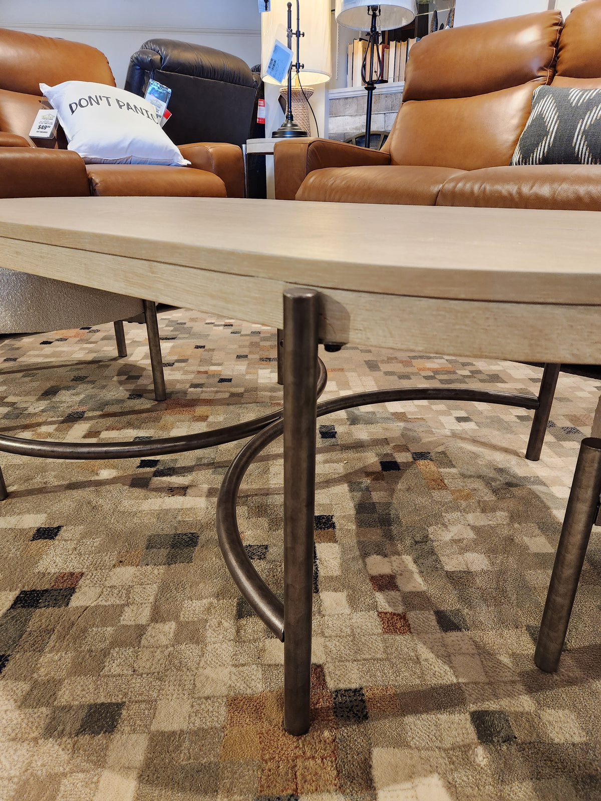 Modern living room with brown leather chairs, Magnussen T5927 Jennings Oval Coffee Table, and a geometric rug.