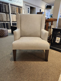 The Handstone Belmont Wing Back Chair with sturdy oak legs is in a showroom, surrounded by fabric samples.