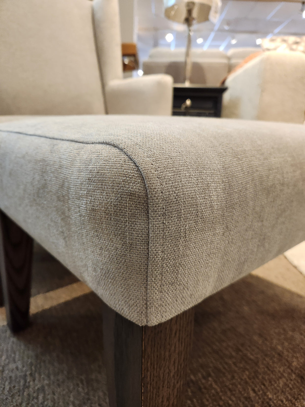 Belmont Ottoman by Handstone: Close-up of rhino fabric corner with oak legs on a carpet in a well-lit store.