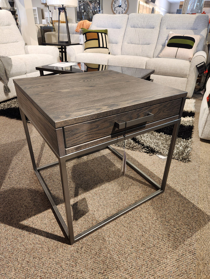 The Muskoka 24" End Table by Handstone, with a solid oak top and metal base, is displayed with beige recliners in the showroom.