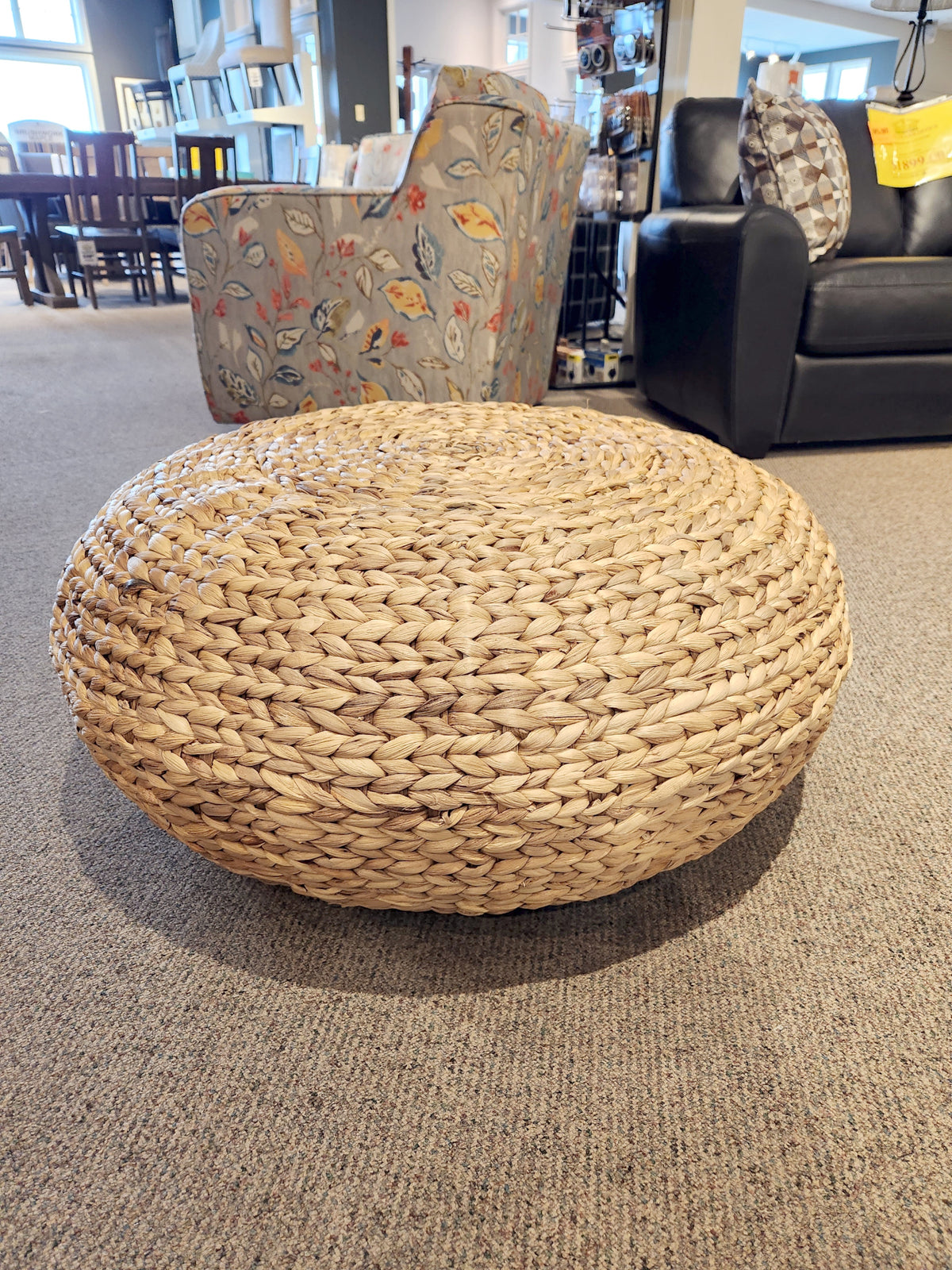 Galice Woven Cocktail Table by Ashley on carpet in a store, surrounded by chairs and shelves.