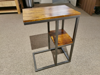 The Forestmin A4000049 Accent Table by Ashley, featuring a rectangular rustic wood top and a lower shelf supported by a black metal frame, sits elegantly on the carpeted floor.