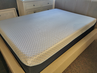 In a cozy bedroom setting, the bed is impeccably made featuring an Ashley Chime Elite Memory Foam Mattress with a white checkered cover and dual ventilation technology for enhanced temperature regulation.