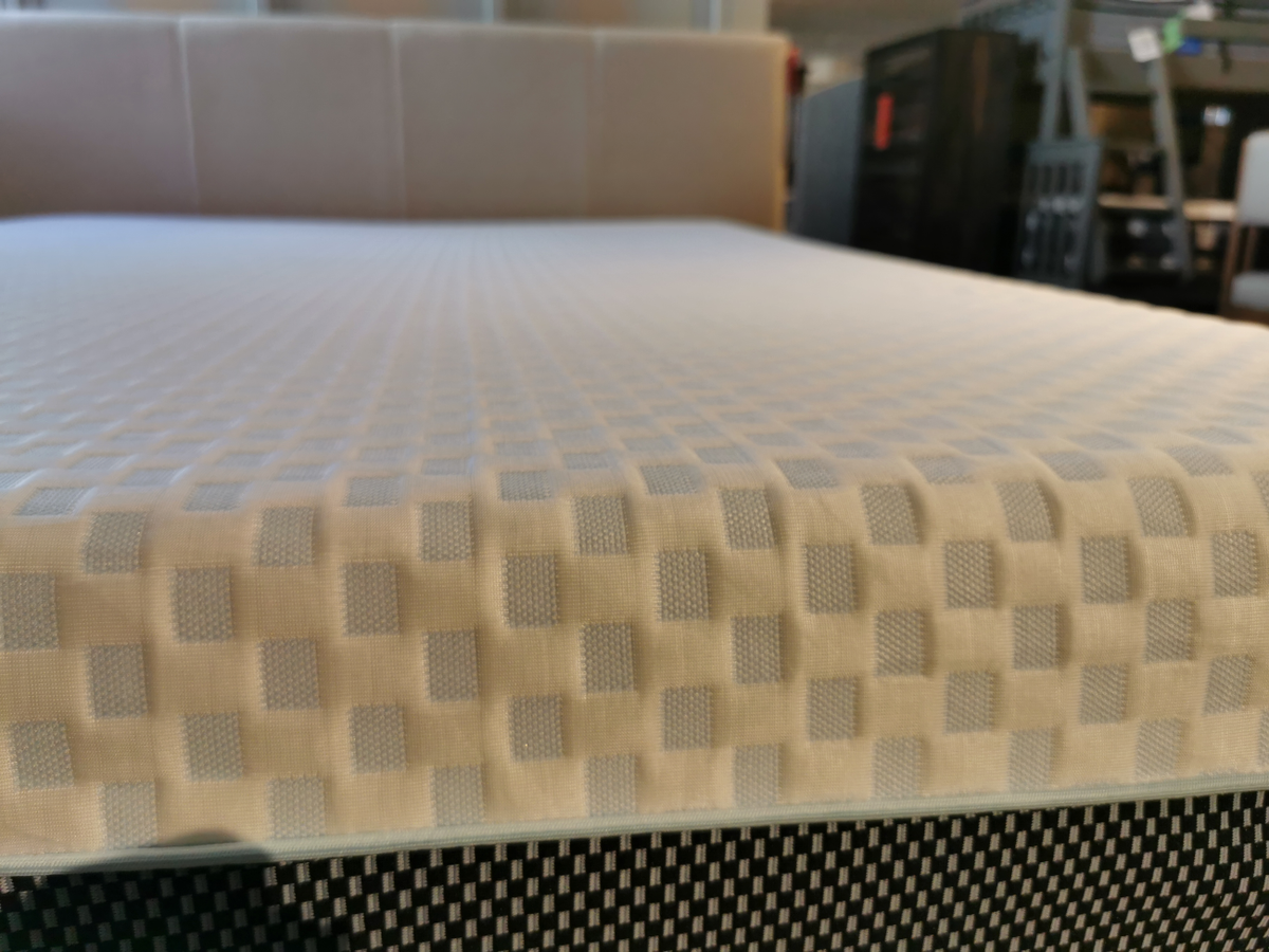 A close-up of the Chime Elite Memory Foam Mattress by Ashley in a showroom, showcasing its checkered pattern and advanced temperature regulation, with blurred furniture visible in the background.