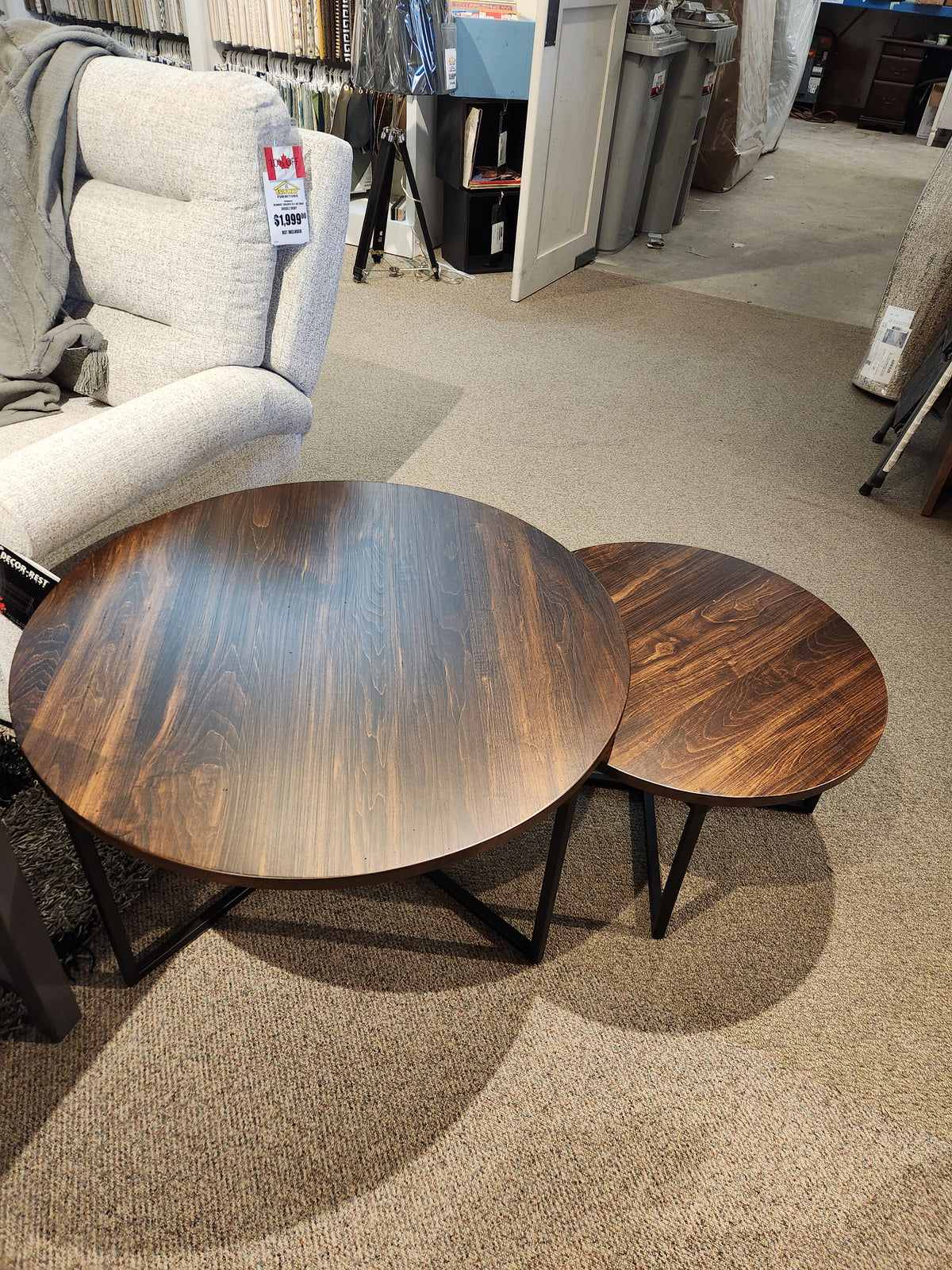 The Alacarte Bedford Round Coffee Table by Handstone features wooden tops and metal frames beside a grey armchair.