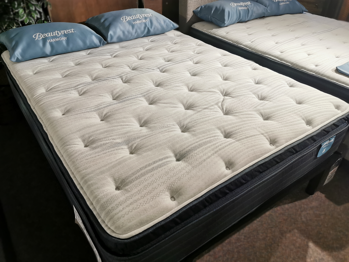 A white quilted Beauty-rest Alcove Medium Pillow Top mattress and two pillows on a showroom floor.