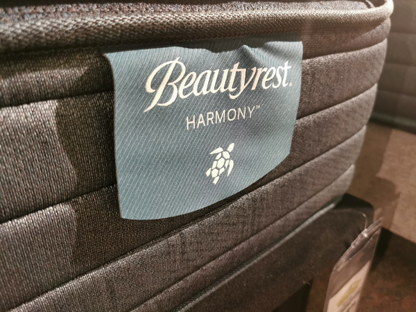 Close-up of a Beauty-rest Alcove Medium Pillow Top mattress label with a turtle icon on textured fabric.