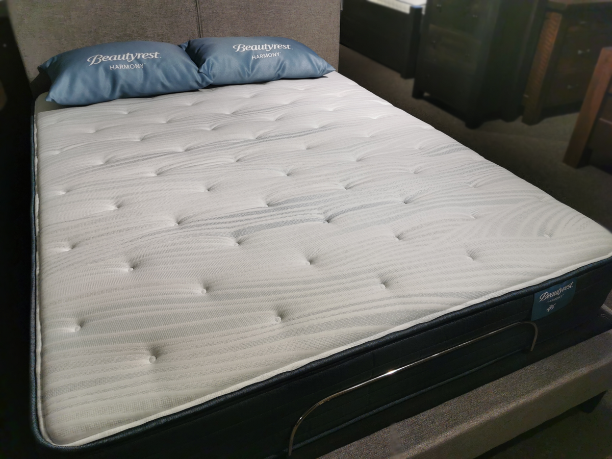 A white Beauty-rest Anchorage TT Mattress with a quilted surface rests on a bed frame, providing the ideal foundation for firm support and restorative sleep. It features two branded blue pillows, perfectly complementing the setup.