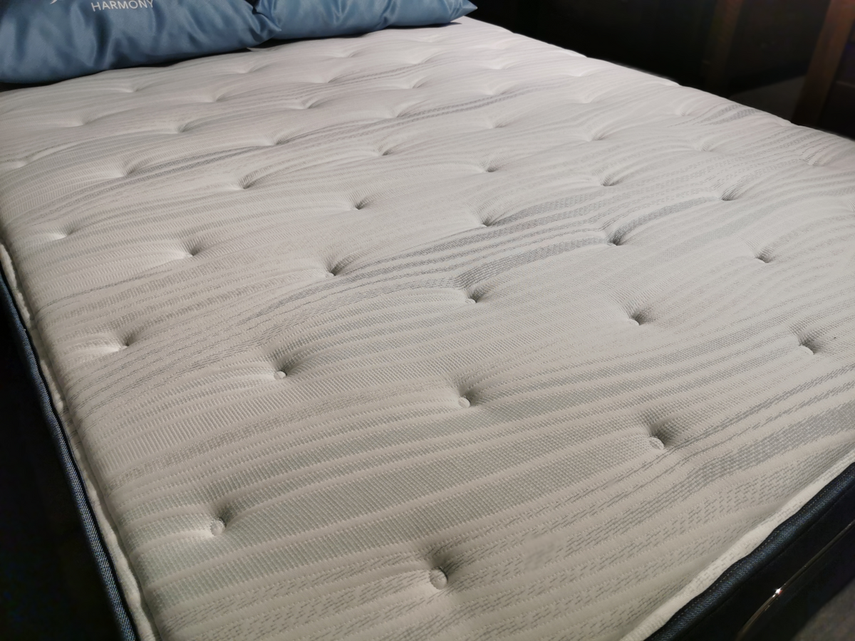 Close-up of a neatly made bed featuring the Beauty-rest Anchorage TT mattress with a white quilted cover and blue pillows, promising restorative sleep.