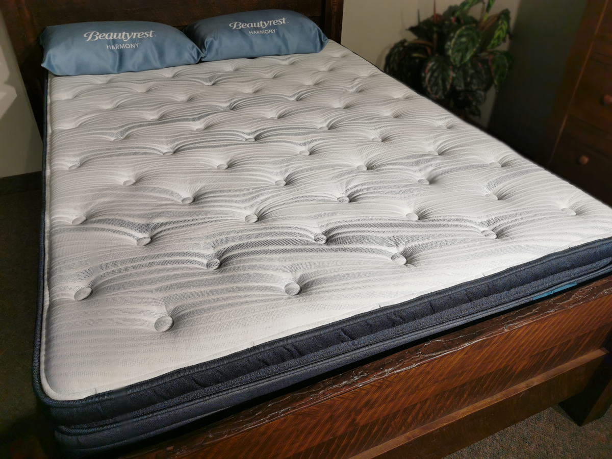 A neatly made bed with a white, quilted Beauty-rest Deepwater Pillow Top Plush Mattress and two matching pillows.