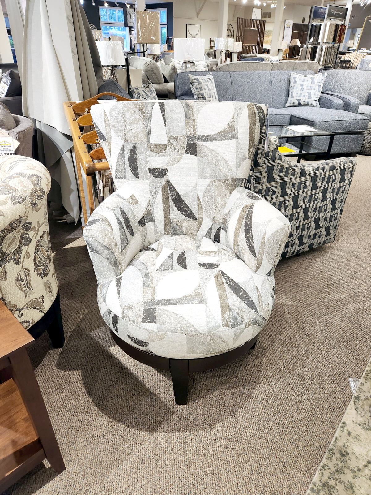 2968E Justine Swivel Chair by Best with abstract fabric on beige carpet, other swivel chairs visible in store background.