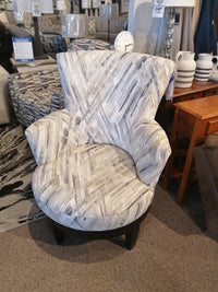 A gray "2968E Justine Swivel Chair" from Best, featuring patterned fabric with a clock placed on it and more furniture nearby.