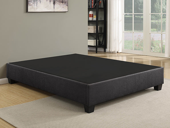 A low-profile EZ Upholstered Bed Frame by Primo, with an elegantly upholstered bed base in black and grey, is placed in a modern room with a light carpet and large windows.