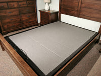 In a carpeted room, a wooden bed frame with the Fashion S-122 Adjustable Base and a mattress foundation is accompanied by a nightstand with a lamp and a dresser.