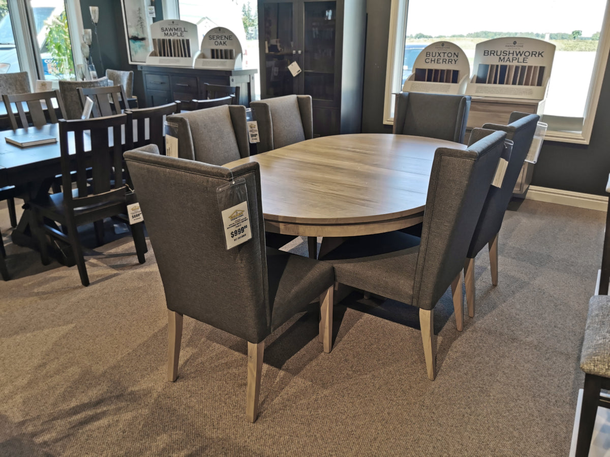 A showroom displays the Handstone JA48 Jasper Dining Package: a round wooden table with six gray upholstered chairs.