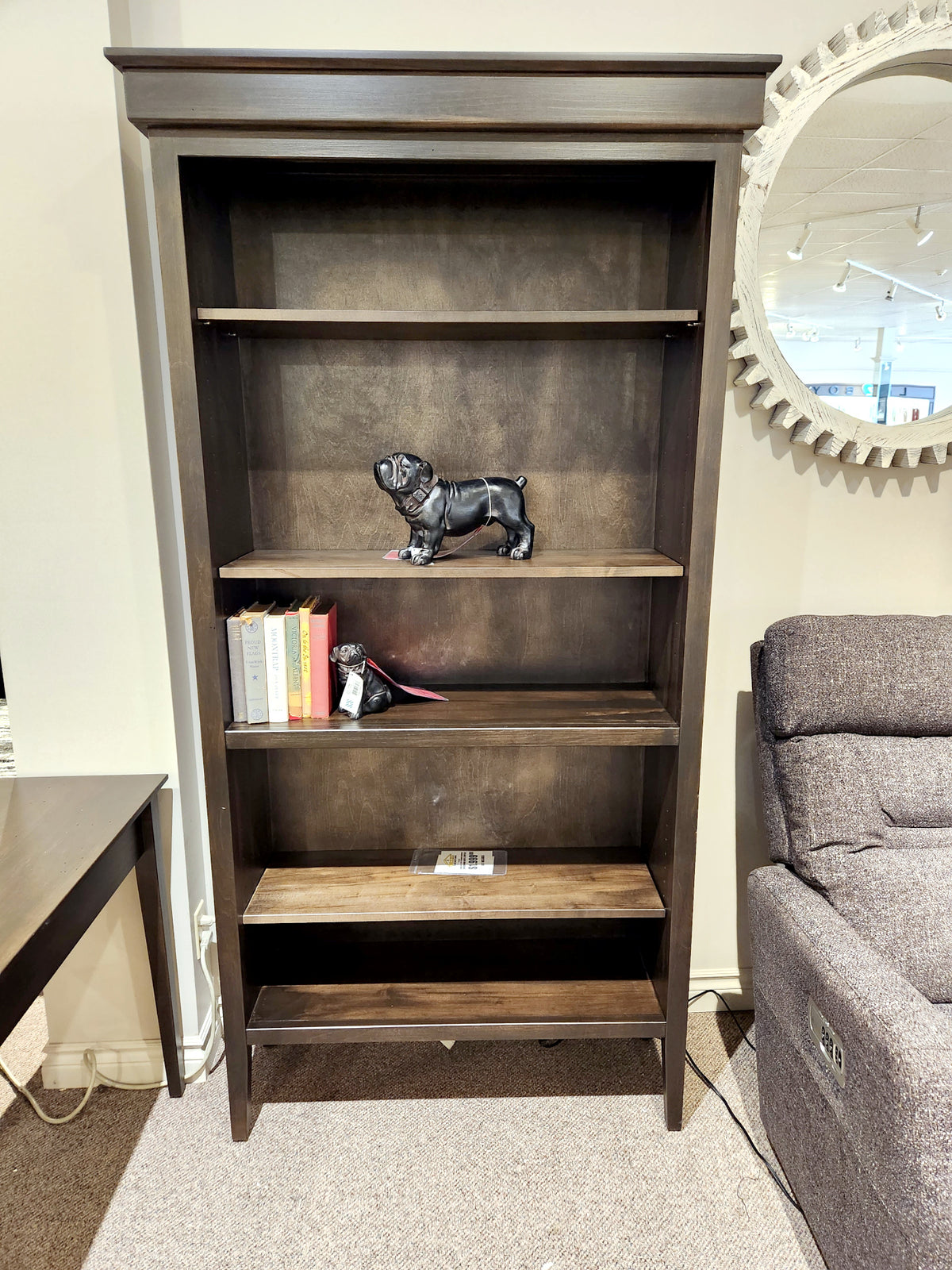 The Handstone 80 Stockholm Bookcase, exemplifying Scandinavian high design, stands gracefully between a mirror and a sofa, adorned with two bulldog figurines and a few cherished books.