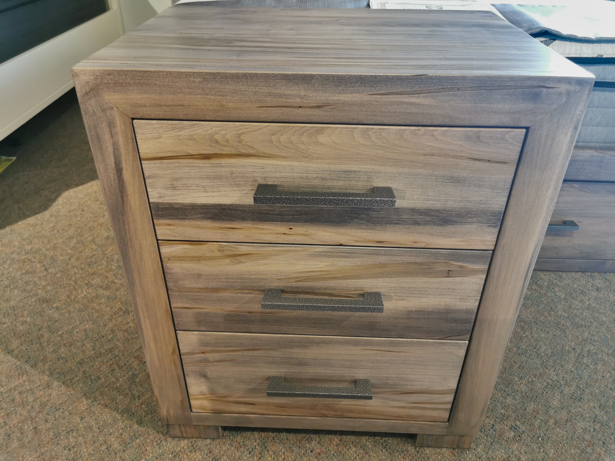 Handstone's Steel City 3 Drawer Night Stand on a carpeted floor, features distressed wood and black handles.