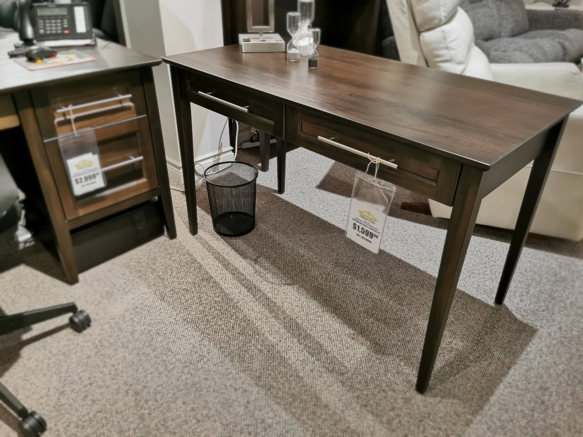 A Handstone ST2448 Stockholm Writing Desk made of dark wood with two drawers is displayed in a store, priced at $189.99, accompanied by a chair on the left side.