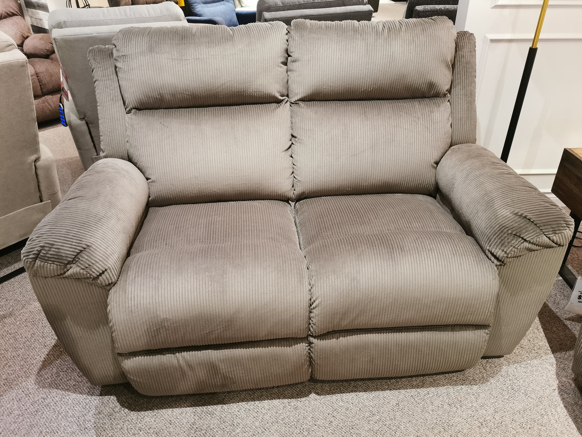 The 761 Joel Reclining Loveseat by La-z-boy, featuring plush gray corduroy upholstery and cushioned arm pads, is displayed on a beige carpet in a furniture showroom.