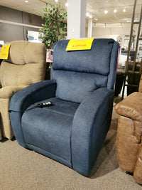 The Evren UC-798-MED Power Lift Chair by Golden, a blue upholstered recliner featuring HeatWave Technology, is on display in the furniture store showroom with a price tag of $2,499.