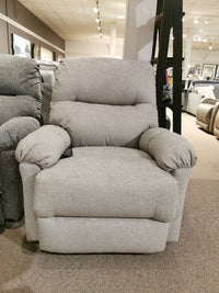 In a furniture store showroom, the 7MP84 Ellisport Power Space Saver Recliner by Best showcases its gray fabric design, featuring soft cushions and wide armrests for ultimate comfort. The recliner also includes a convenient 2-button remote for effortless adjustments.