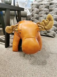 Reiner's Originals Brown Leather Moose Ottoman with fabric antlers sits on the carpeted floor near the coffee table.