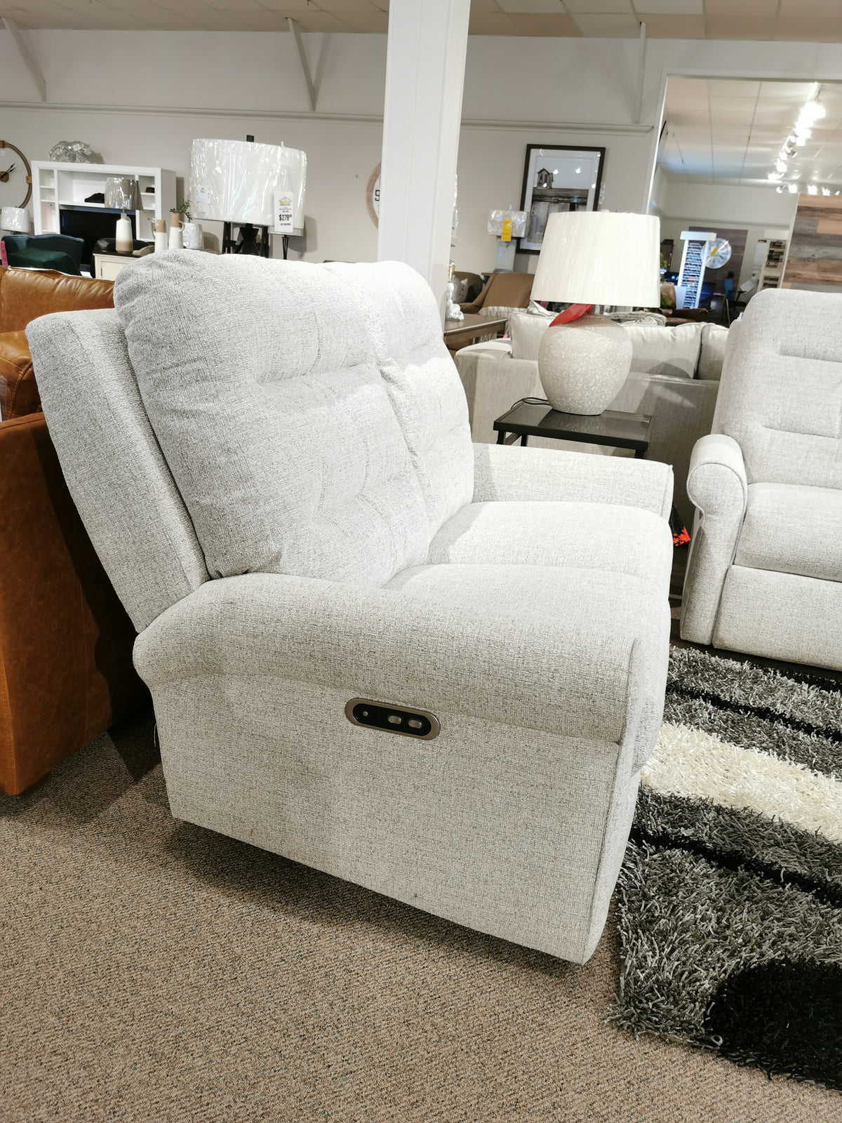 The showroom floor features the Decor-rest M8508 Power Reclining Loveseat, complete with traditional arms and headrest lumbar support, surrounded by other elegant furniture and decor items in the background.