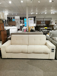 The Mathias Queen Sofa Bed by Donald Choi, featuring high-density foam seats and a soft, cream-colored texture, is on display in a furniture store showroom.