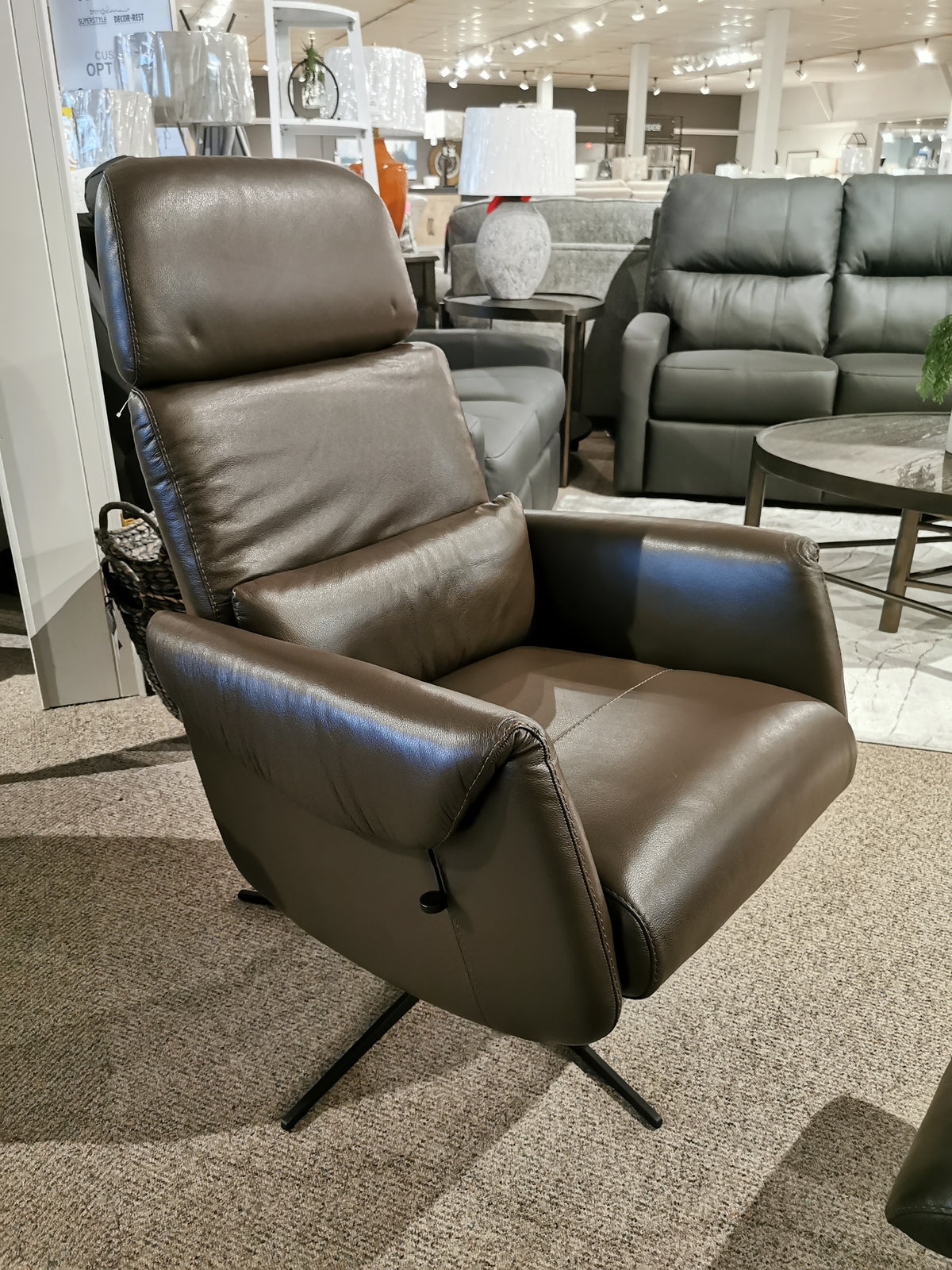 Licia Recliner with Ottoman by Donald Choi displayed in a furniture showroom, featuring a smooth motion mechanism, with elegant sofas in the background.