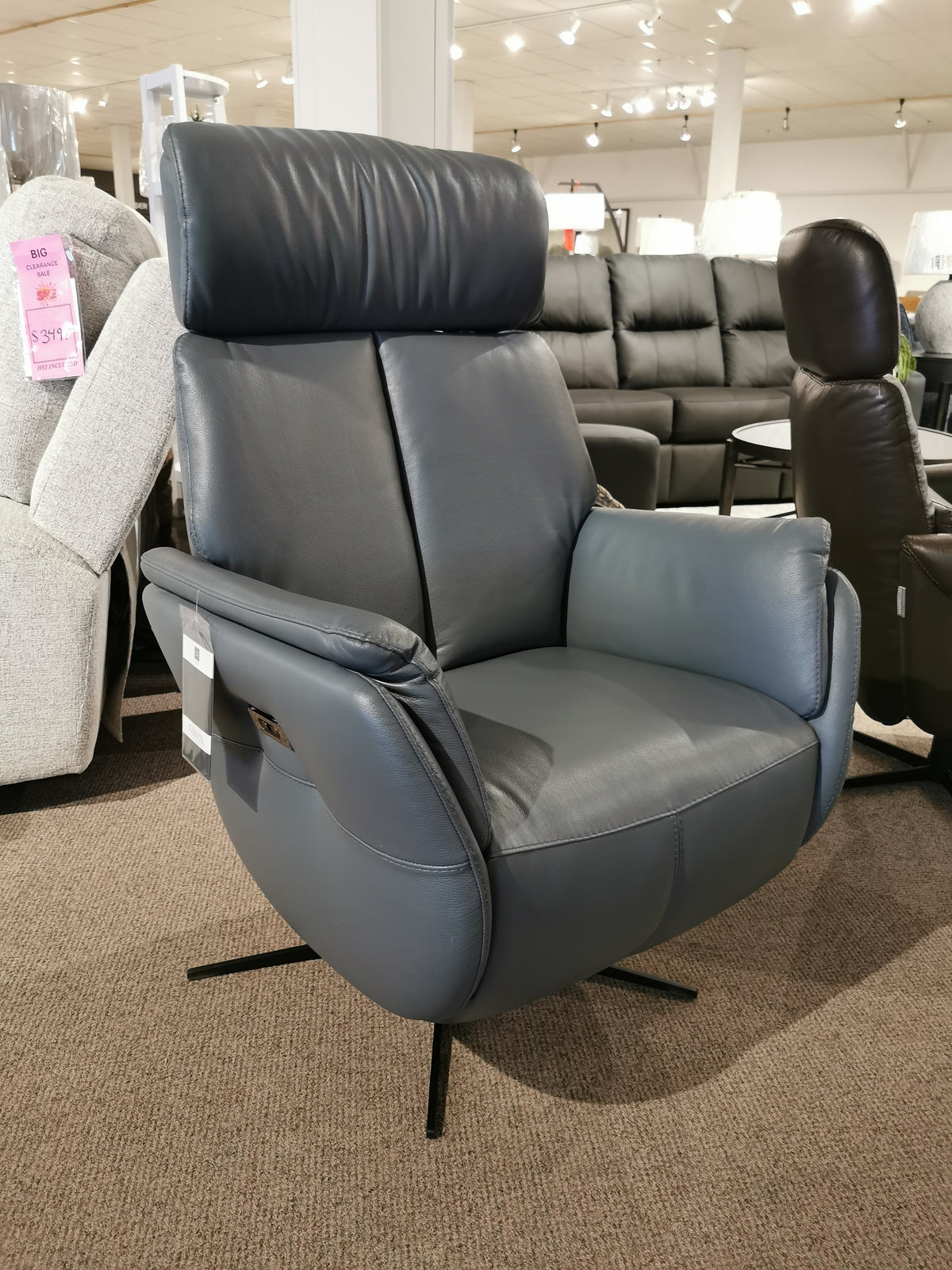 On a showroom floor, the dark gray Argo Power Recliner by Donald Choi, featuring an elegant swivel mechanism, stands out amidst an array of other exquisite furniture pieces in the background.