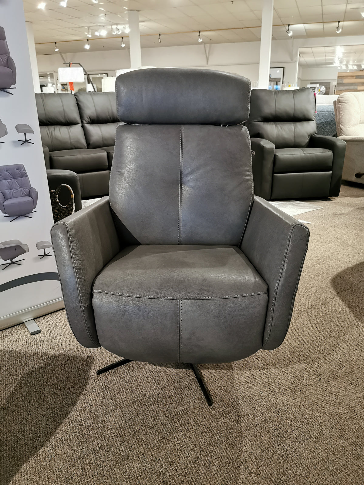 An Artu Power Recliner by Donald Choi, crafted from gray Italian leather and equipped with a smooth motion mechanism, sits elegantly in a showroom with other furniture on display.