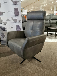 Donald Choi's Artu Power Recliner, crafted in gray Italian leather and featuring a headrest, is showcased in a showroom with posters and additional seating visible in the background.