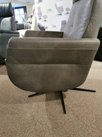 Artu Power Recliner by Donald Choi on a carpeted floor, showcasing a sleek motion mechanism. In the background, a poster features various chair models.