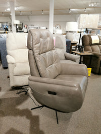 The Vega Power Recliner by Donald Choi, an elegant gray chair made from premium Italian leather and equipped with control buttons, is showcased in a furniture store showroom among other chairs.