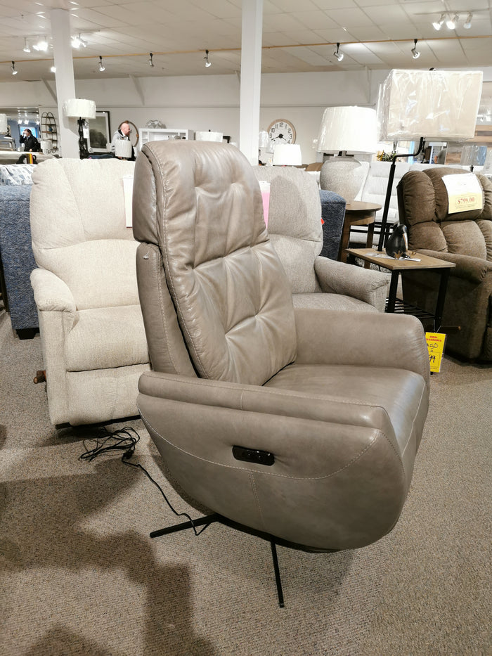 The Vega Power Recliner by Donald Choi, an elegant gray chair made from premium Italian leather and equipped with control buttons, is showcased in a furniture store showroom among other chairs.