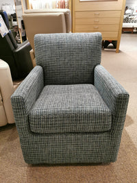 A blue textured upholstered Pia Swivel Chair from the Palliser brand sits elegantly on a carpeted floor in a furniture store, showcasing its versatile design.