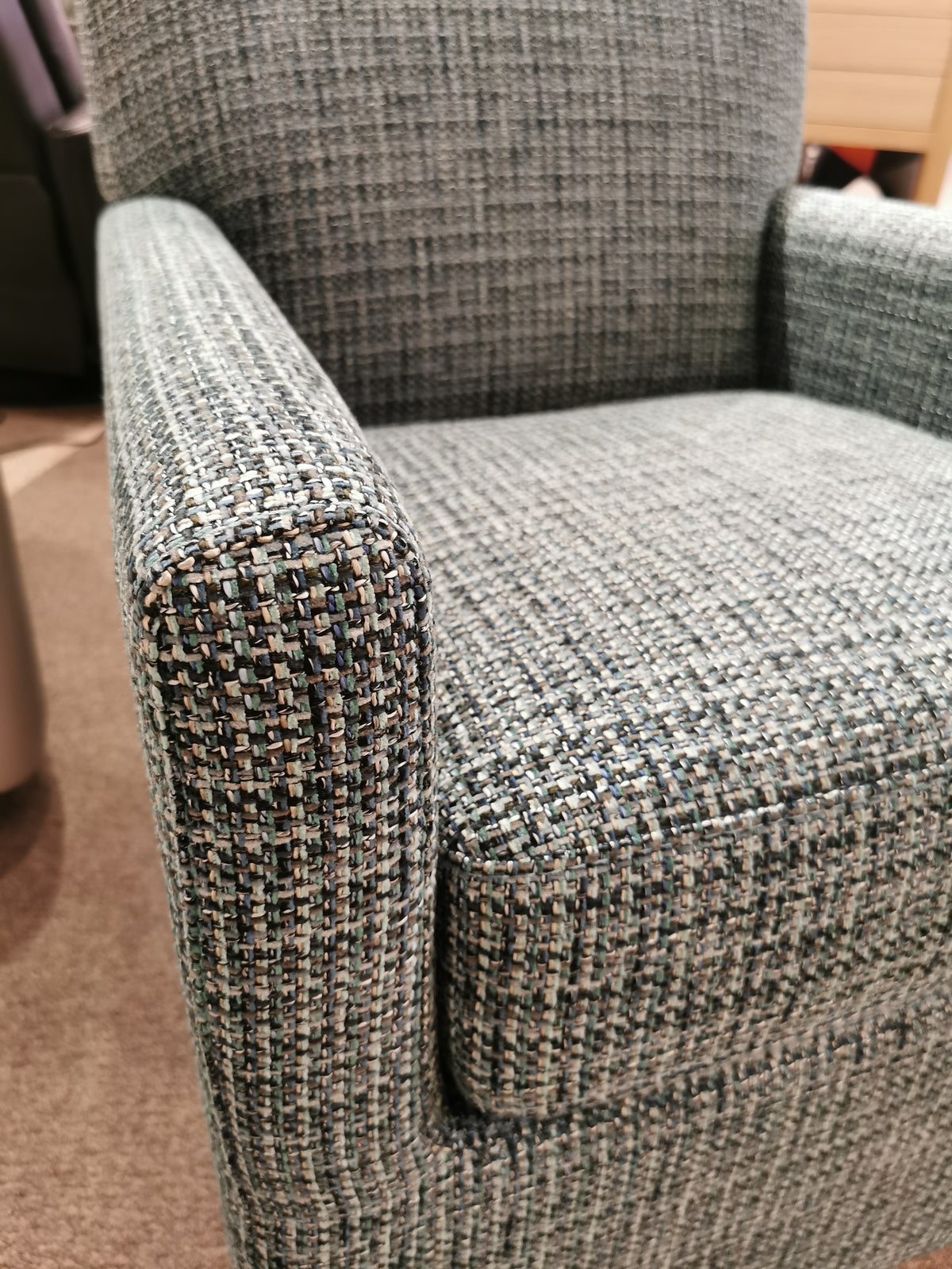 Close-up of the Pia Swivel Chair from Palliser, showcasing its blue-and-gray upholstery with textured fabric and padded armrests. Its minimalist shape and versatile design make it an ideal addition to any carpeted floor space.