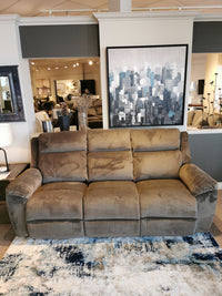 In a showroom, the 761 Joel Power Reclining Sofa by La-z-boy elegantly sits on top of a blue and white rug, complemented by cityscape artwork adorning the wall behind it. The cushioned arm pads beckon for relaxation.